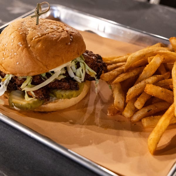 A Runaway Train Brewery fried chicken sandwich with pickles and slaw, served with fries on a metal tray.