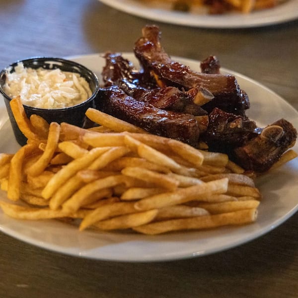 Runaway Train Brewery's BBQ ribs with a side of golden fries and coleslaw on a white plate.