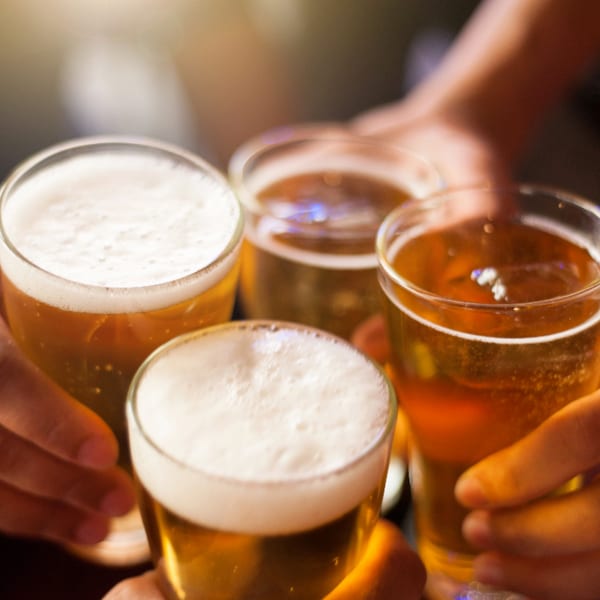 Four hands holding up glasses of Runaway Train Brewery beer, clinking in a toast.