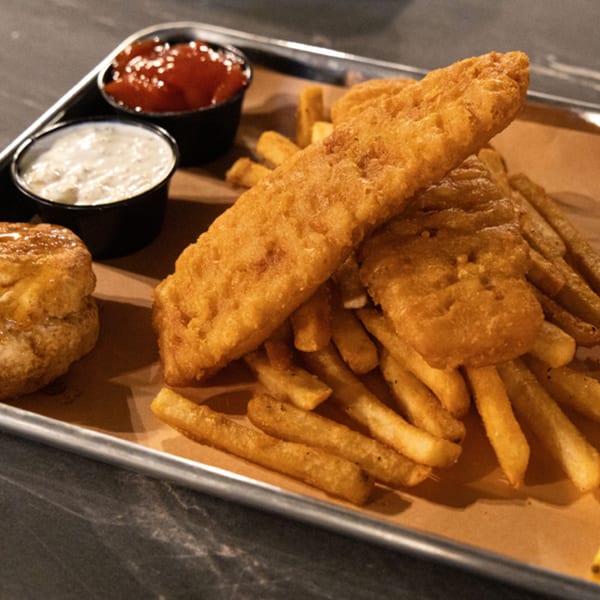 Golden-brown fish and chips with a biscuit, ketchup, and tartar sauce on a metal tray.