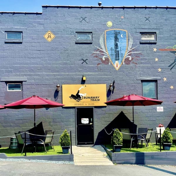 Exterior of Runaway Train Brewery with a mural, red umbrellas, and outdoor seating on artificial turf.