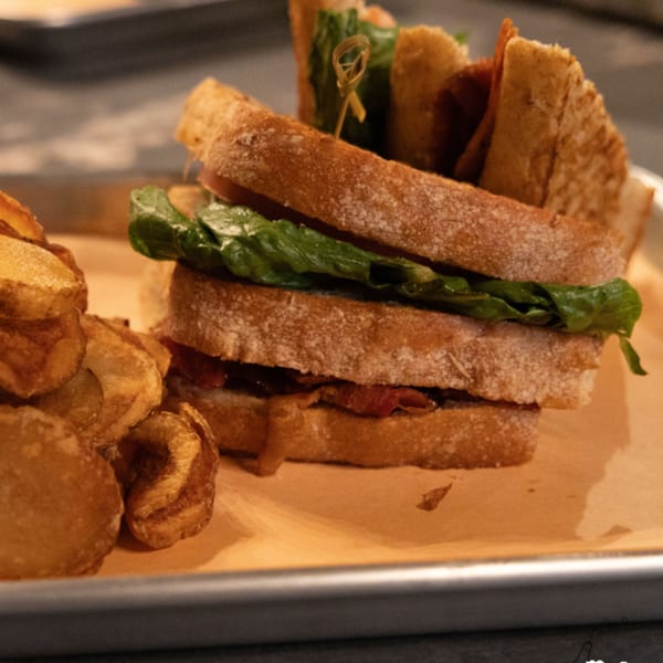 A Runaway Train Brewery sandwich with bacon, lettuce, and crispy chips on a metal tray.