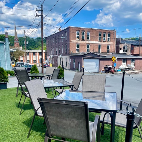 Outdoor patio seating with glass tables and chairs on artificial turf, surrounded by urban buildings.